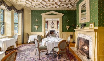 An opulent dining room at The Erlowest, featuring beautiful interiors, tables set for dinner and a fireplace.