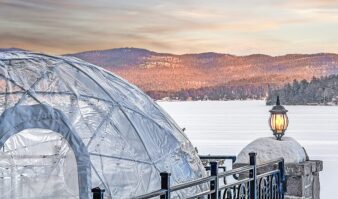 A glass igloo sitting on the edge of a lake.