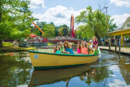 A group of people in a small yellow boat glides along a calm waterway, with the thrilling rides of Six Flags visible in the background.