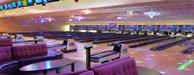 Modern bowling alley with multiple lanes, colorful seating, and overhead screens displaying information. Vibrant lighting creates a lively atmosphere.