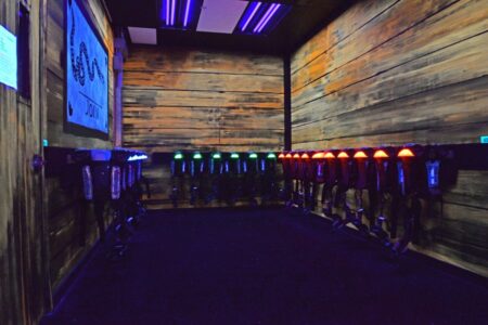 A dimly lit room with rows of glowing laser tag vests hanging on wooden walls, reminiscent of the vibrant energy at Lanes & Games.